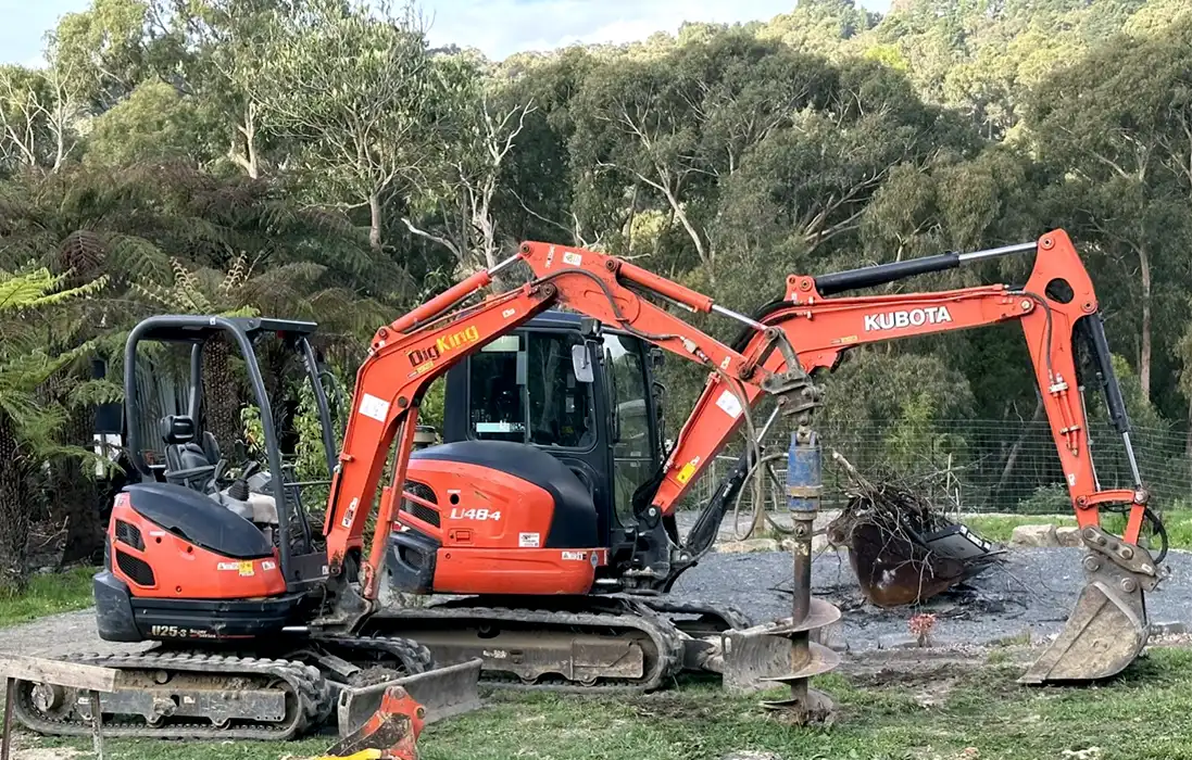 Two orange excavators parked on a dirt road, ready for excavation jobs.